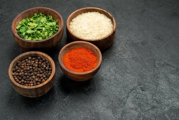 Zijaanzicht kruiden op tafel kruiden kruiden rijst en zwarte peper in kommen aan de linkerkant van de zwarte tafel