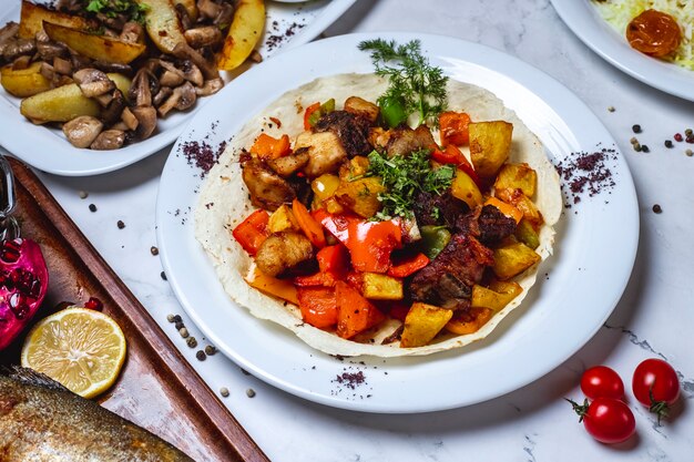 Zijaanzicht lamsgebraad met gegrilde rode en gele paprika's, aardappelgreens en tomaat op tafel