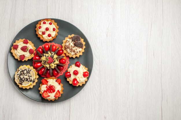 Zijaanzicht linksboven chocoladetaart afgerond met bessentaartjes in de grijze plaat in het midden van de witte houten tafel