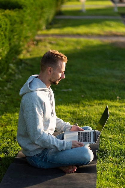 Zijaanzicht man zit in de lotushouding tijdens het werken op laptop
