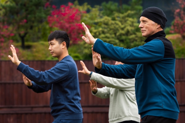 Gratis foto zijaanzicht mensen die tai chi buiten beoefenen