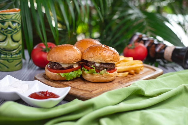 Zijaanzicht mini hamburgers rundvlees patty tomatensla kaas ketchup en frietjes op een bord