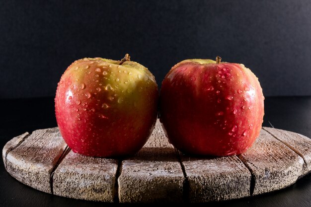 Zijaanzicht natte rode appels op witte houten bord op zwarte horizontaal