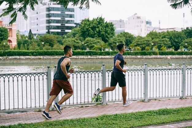 Zijaanzicht over de volledige lengte van twee jongens die bij de rivier op de brug joggen