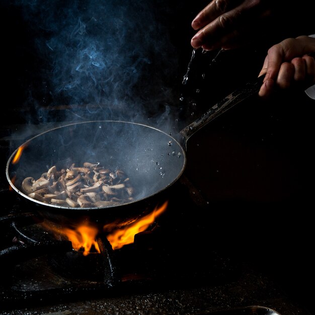 Zijaanzicht paddenstoel bakken met waterdruppel en vuur en mens hand in pan