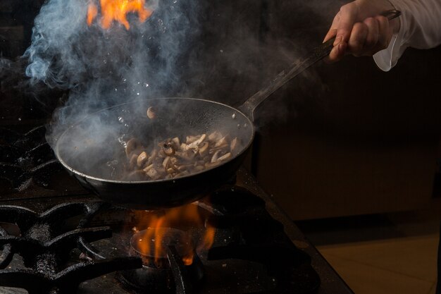 Zijaanzicht paddestoel bakken met rook en vuur en menselijke hand en pan in de kachel