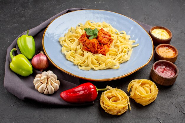 Zijaanzicht pasta en sauzen bord pasta met vlees en jus pasta bal peper knoflook ui naast de kommen sauzen op het tafelkleed