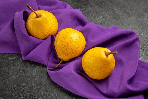 Zijaanzicht peren op het tafelkleed drie gele peren op het paarse tafelkleed op de donkere tafel