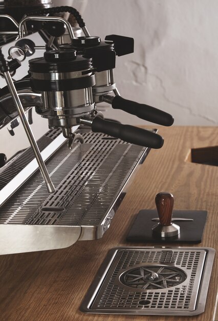 Zijaanzicht professionele chromen koffiemachine met twee koppen en geladen portafilters in caféwinkel op houten dikke tafel en stamper op lederen padespresso, cappuccino, latte maker.