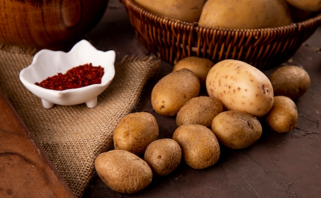 Zijaanzicht rauwe aardappelen met chili vlokken op bruine achtergrond