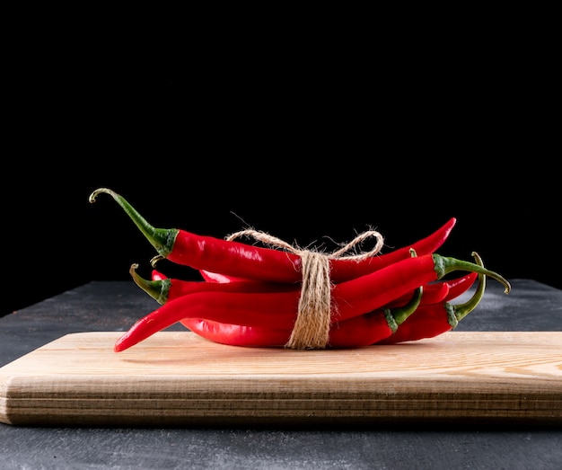 Zijaanzicht rode chili peper op houten snijplank op zwart