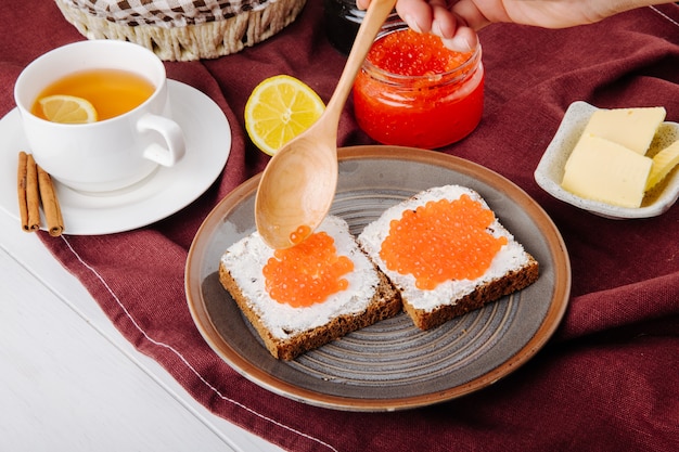 Zijaanzicht rode kaviaar toast roggebrood met cottage cheese rode kaviaar boter kopje thee en schijfje citroen op tafel