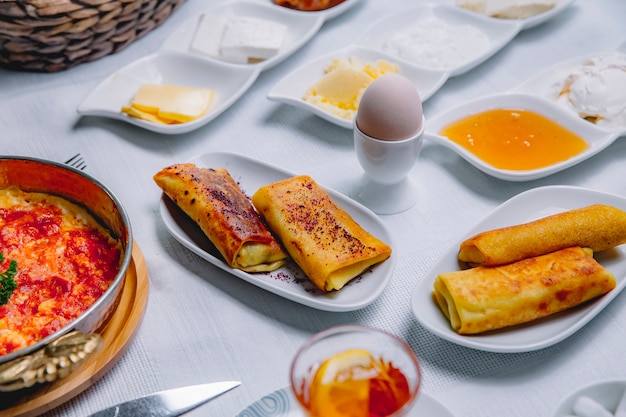 Zijaanzicht rolde pannenkoeken met gekookt ei en honing op tafel geserveerd ontbijt