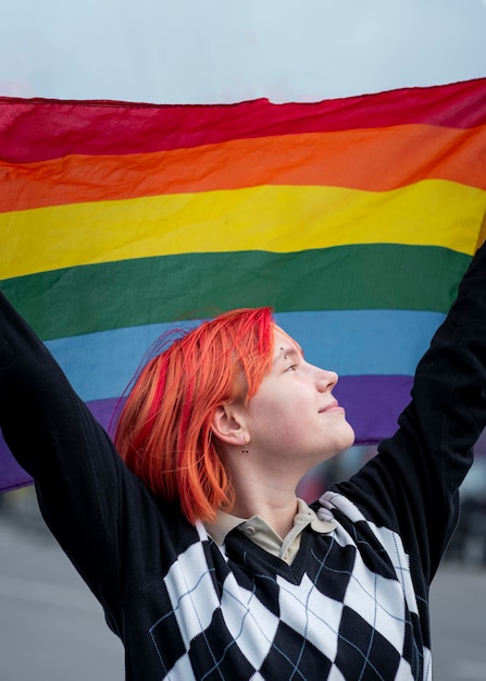 Gratis foto zijaanzicht roodharige niet-binaire persoon die een lgbt-vlag steunt