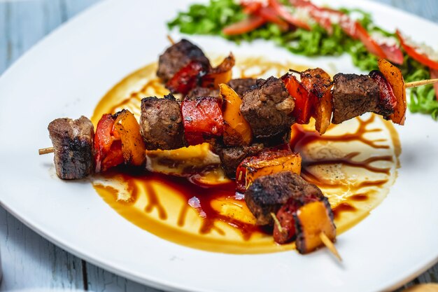 Zijaanzicht rundvlees kebabs gegrild rundvlees met tomaat rode en gele paprika en saus op een plaat