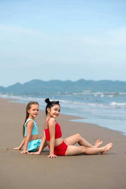 Zijaanzicht smiley meisjes zitten op het strand