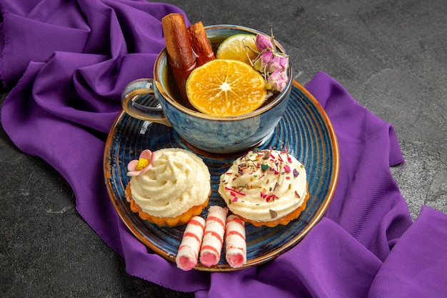 Zijaanzicht snoepjes op tafel cupcakes op het bord en een kopje kruidenthee op het paarse tafelkleed