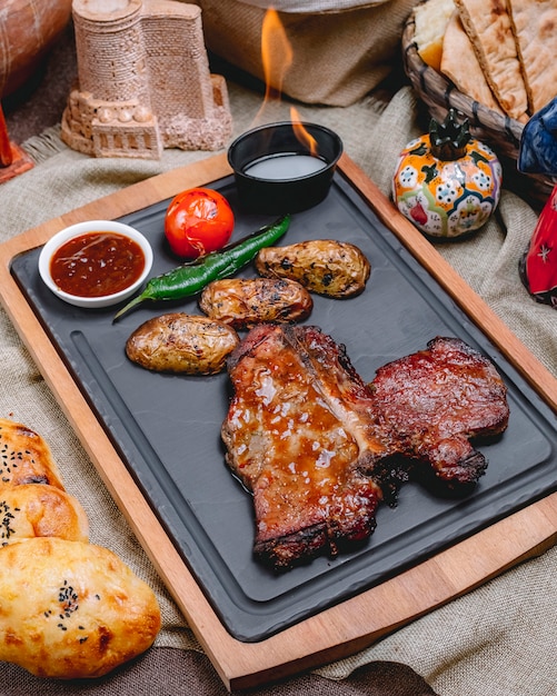 Zijaanzicht steak in saus met aardappelen tomaat en peper met saus op een dienblad