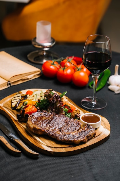 Zijaanzicht steak met gegrilde groenten met saus en een glas rode wijn