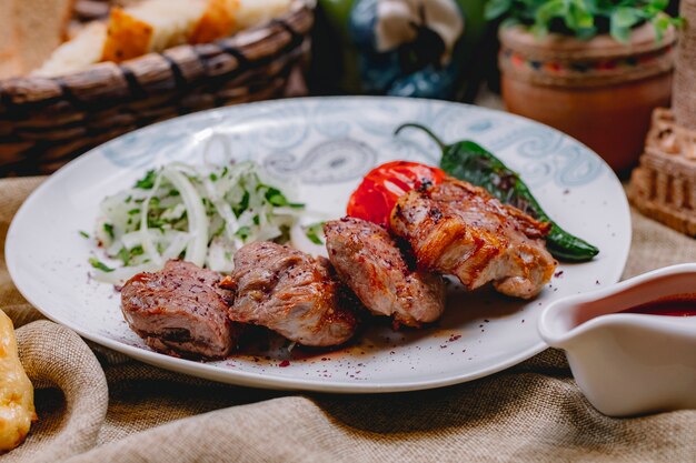 Zijaanzicht tikya kebab met de gegrilde ui van de tomaten hete peper en greens op een plaat