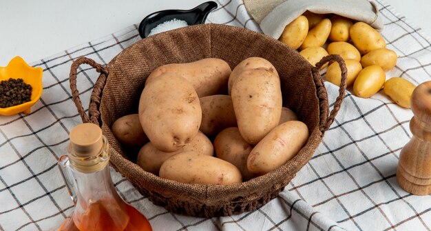 Zijaanzicht van aardappelen in mand met boter zout zwarte peper op plaid doek en witte tafel