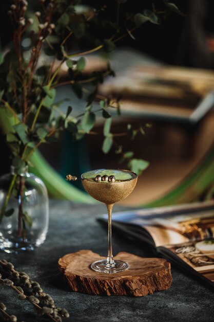 Zijaanzicht van alcoholcocktail met kiwi in een gouden glas op een houten tribune