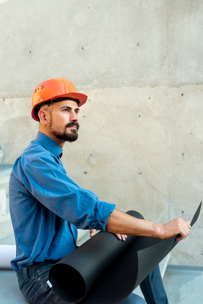 Gratis foto zijaanzicht van architect met helm en blauwdrukken