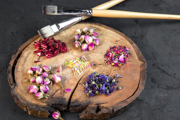 Zijaanzicht van assortiment van droge bloem en roze thee twee borstels op houten bord op zwart