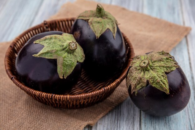 Zijaanzicht van aubergines in mand op zak en op houten achtergrond