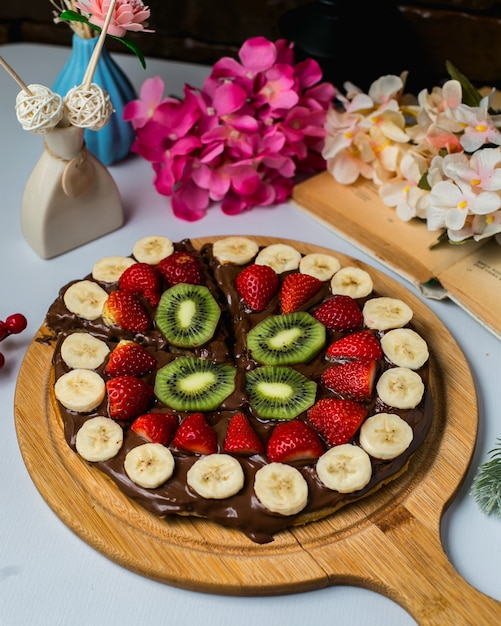 Zijaanzicht van Belgische wafel bedekt met donkere chocolade en fruit op een houten bord