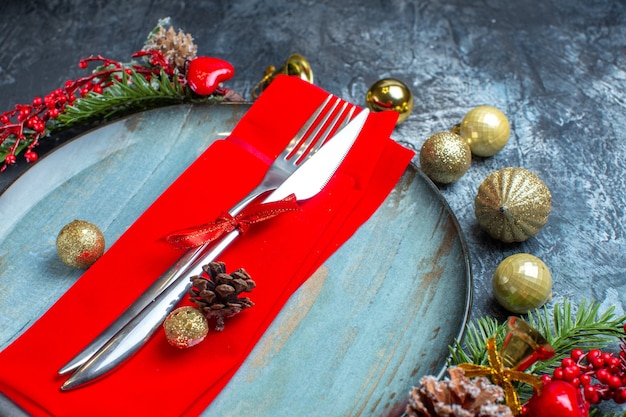 Zijaanzicht van bestekset met rood lint op een decoratief servet op een blauw bord en kerstaccessoires op donkere achtergrond