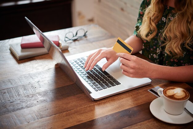 Zijaanzicht van bijgesneden onherkenbare blonde vrouw die plastic kaartinformatie op laptop typen