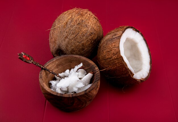 Zijaanzicht van bruine kokosnoten met hele en gehalveerde kokosnootpulp van kokosnoot in een houten kom op rode oppervlakte