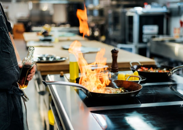 Zijaanzicht van chef-kok die een schotel in de keuken flambeing