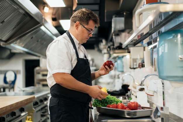 Zijaanzicht van chef-kok die met schort groenten in de keuken controleert