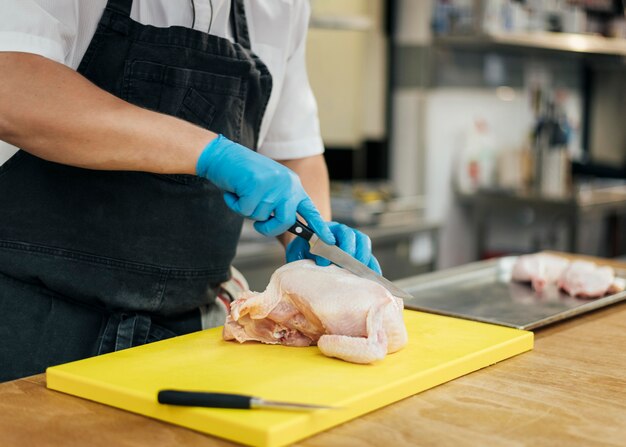 Zijaanzicht van chef-kok met schort en handschoenen die kip snijden