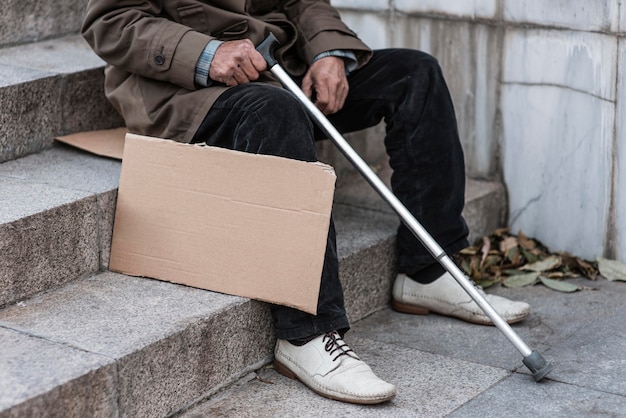 Gratis foto zijaanzicht van dakloze man op trappen met stok en leeg bord