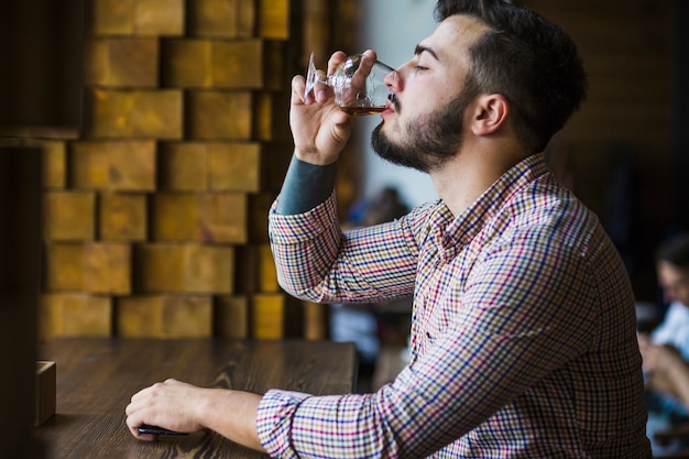 Gratis foto zijaanzicht van de jonge mens die van drank geniet