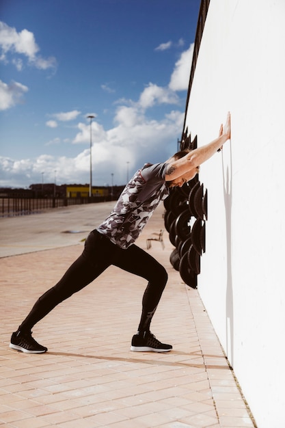 Zijaanzicht van de jonge sportieve man doet push-ups op de muur