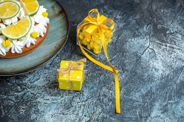 Zijaanzicht van de kerstachtergrond met mooie gele geschenkdozen en cake versierd met citroen op donkere tafel