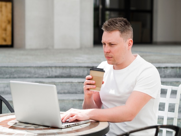 Zijaanzicht van de mens die in openlucht koffie heeft en aan laptop werkt