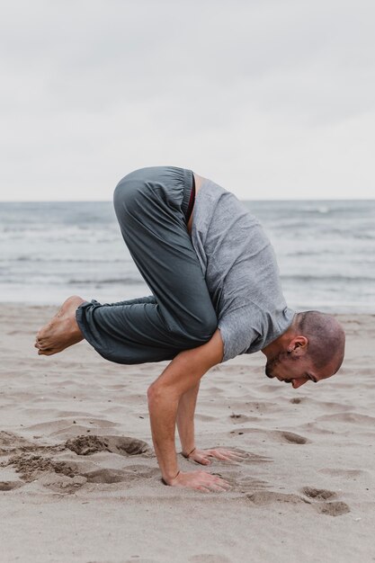 Zijaanzicht van de mens die yogaposities op het strand beoefent