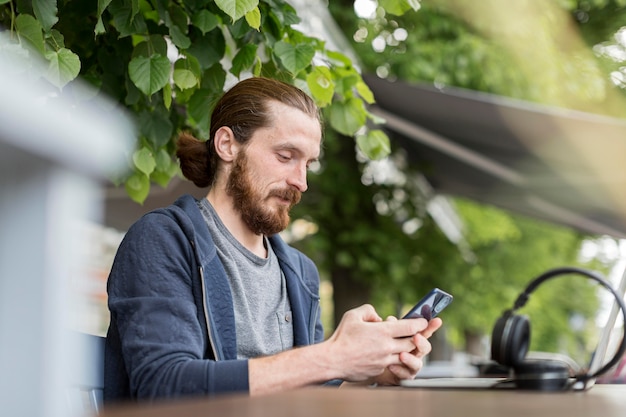 Gratis foto zijaanzicht van de mens in de stad met smartphone en koptelefoon