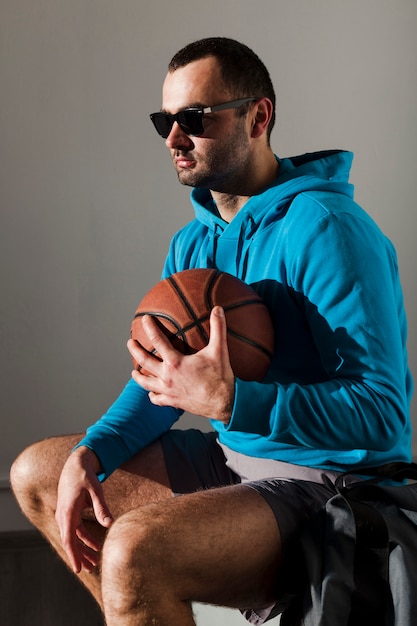Zijaanzicht van de mens in hoodie en zonnebril die basketbal dicht bij borst houden