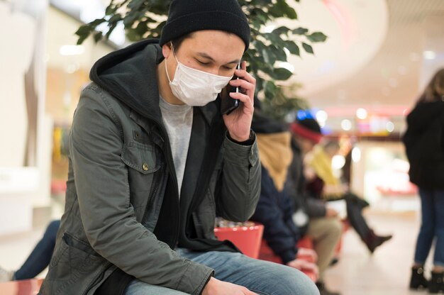 Zijaanzicht van de mens met medisch masker dat op de telefoon bij wandelgalerij spreekt
