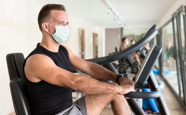 Zijaanzicht van de mens met medisch masker trainen in de sportschool