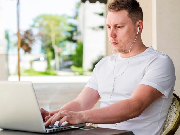 Zijaanzicht van de mens met oortelefoons die aan laptop in openlucht werken