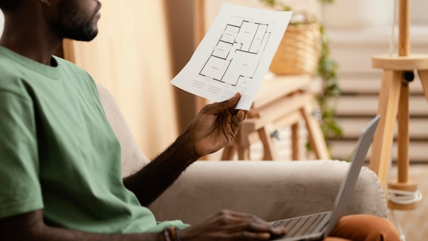 Gratis foto zijaanzicht van de mens op de bank die een plan maakt om huis met laptop opnieuw in te richten