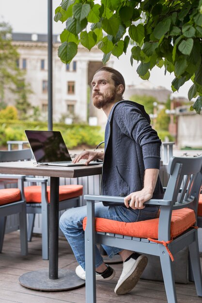 Zijaanzicht van de mens op een stadsterras met laptop