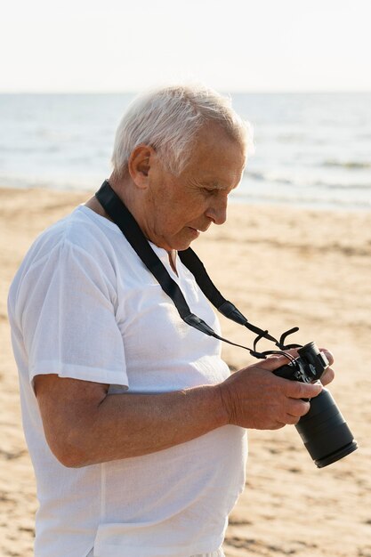 Zijaanzicht van de oudere man met camera aan het strand